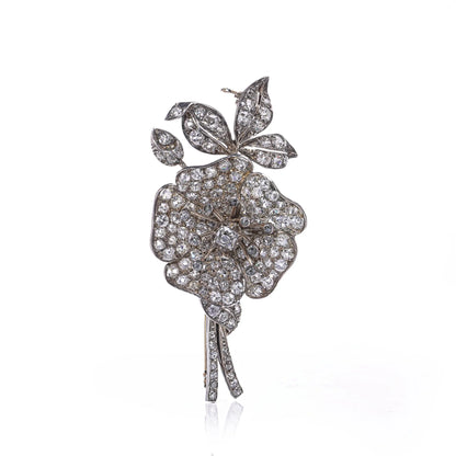 A decorative flower brooch set with diamonds, in silver and gold, on a white background