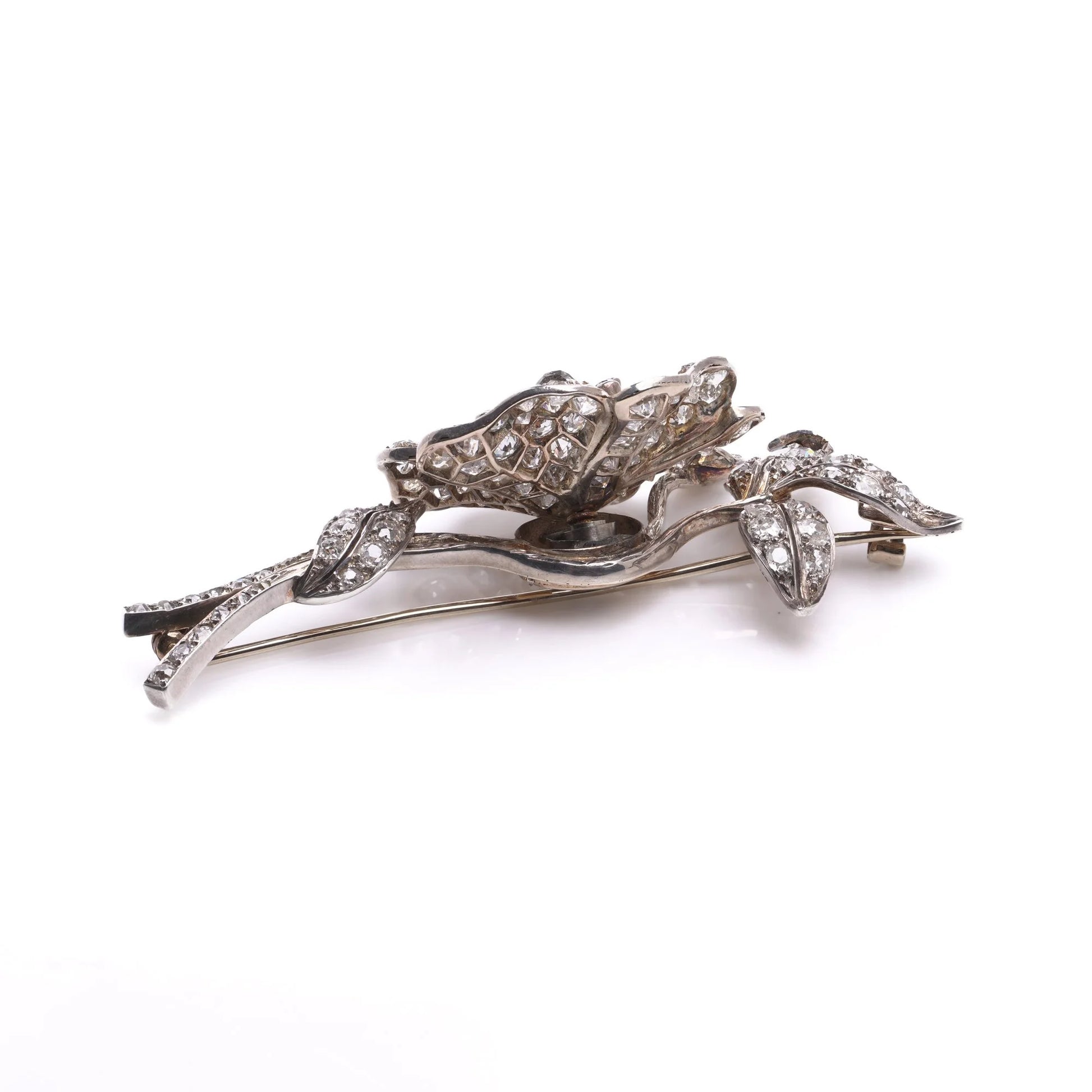 A decorative flower brooch set with diamonds, in silver and gold, on a white background