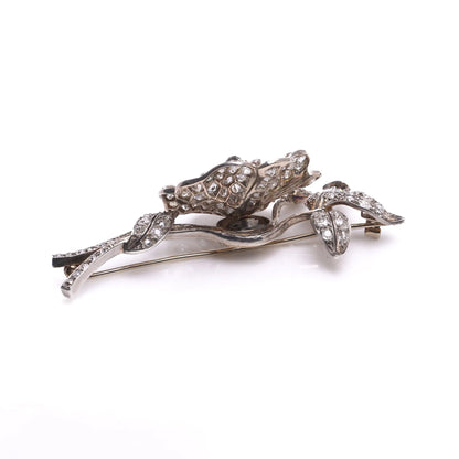A decorative flower brooch set with diamonds, in silver and gold, on a white background