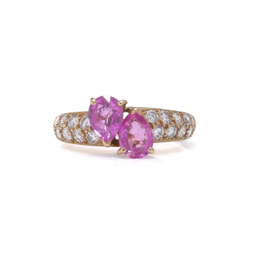 A yellow gold ring with pear shaped pink sapphires and round diamonds, on a white background
