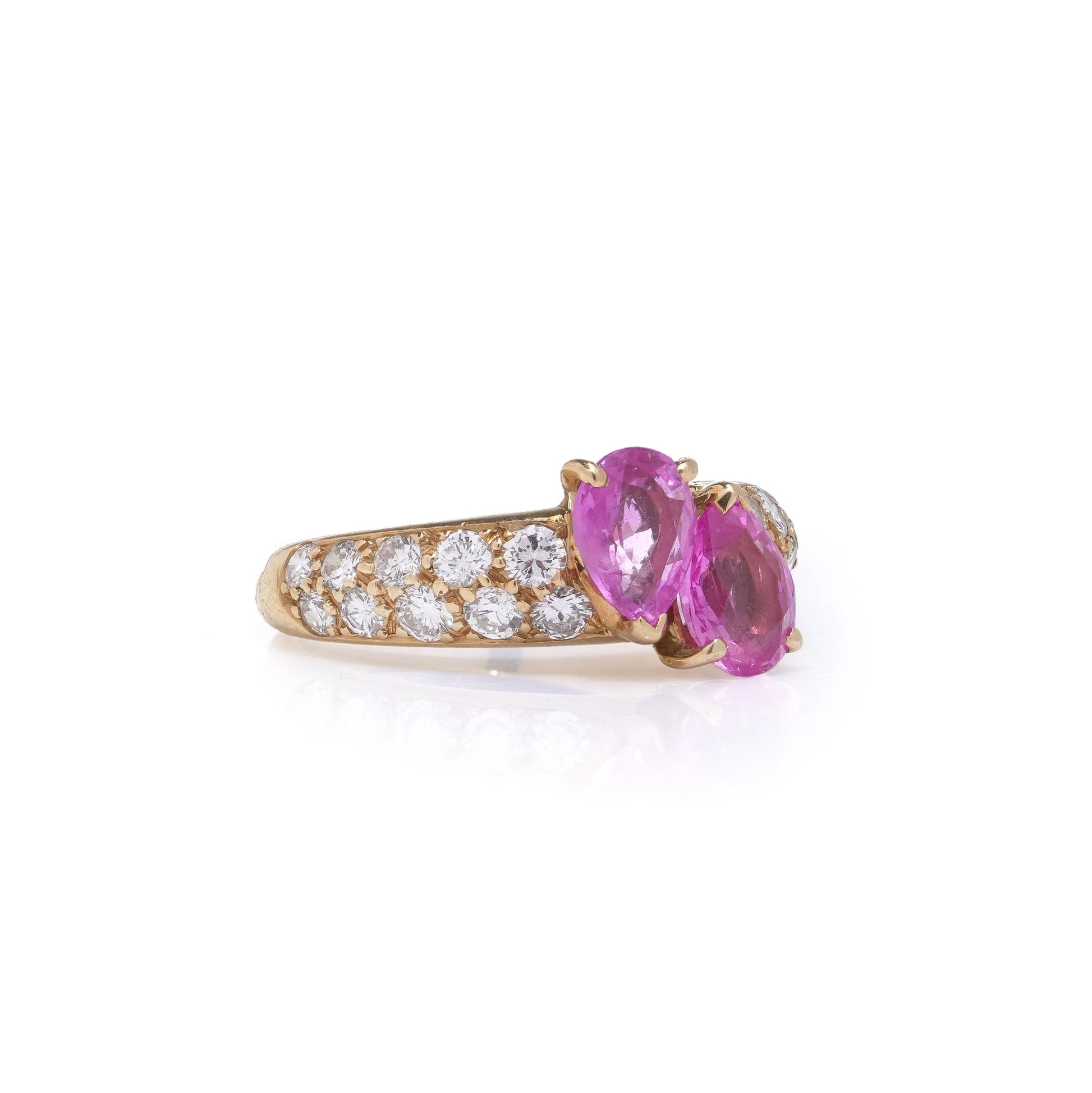 A yellow gold ring with pear shaped pink sapphires and round diamonds, on a white background