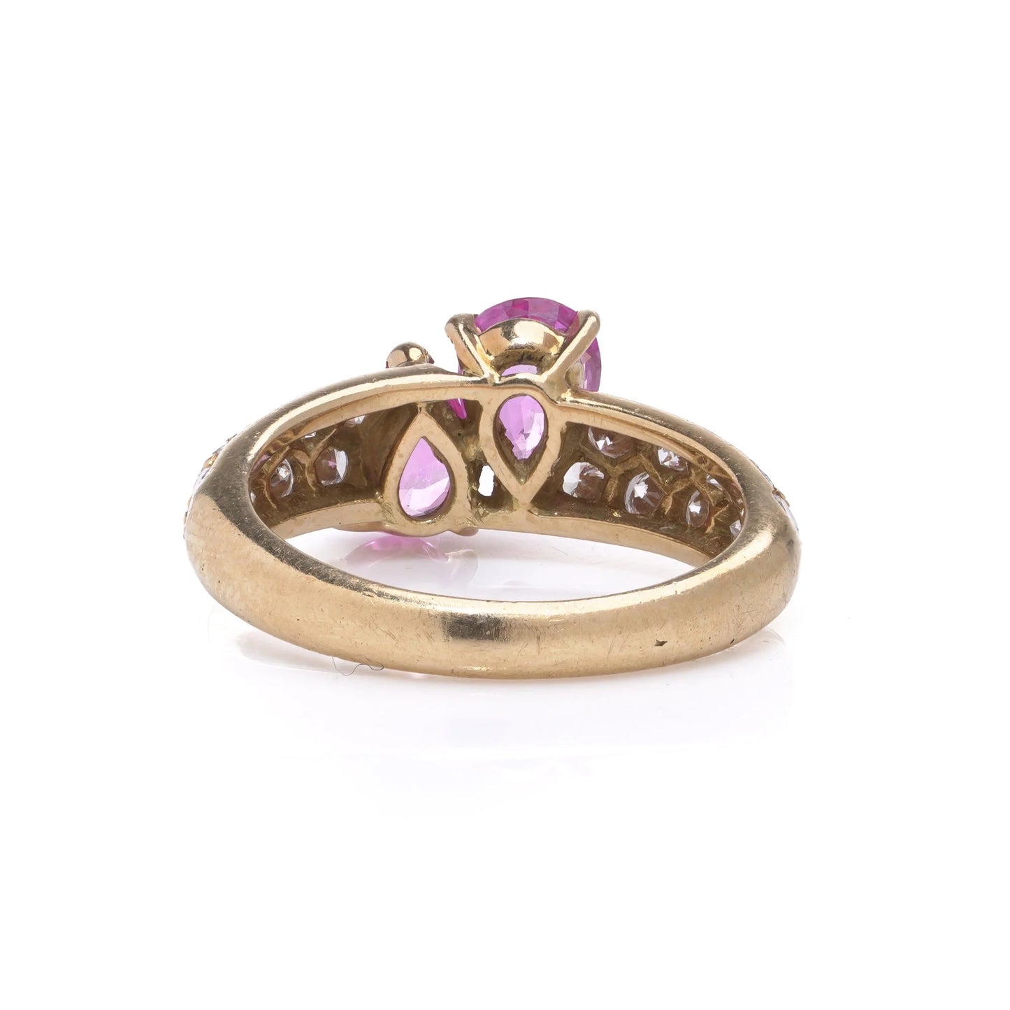 A yellow gold ring with pear shaped pink sapphires and round diamonds, on a white background