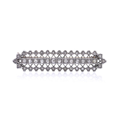 An openwork diamond set bar brooch in gold and silver, on a white background