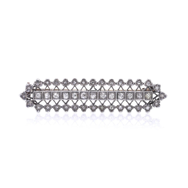 An openwork diamond set bar brooch in gold and silver, on a white background