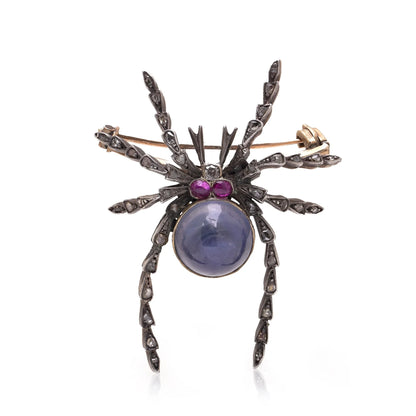 A spider brooch with a sapphire and ruby body and diamond legs, in silver and gold, on a white background
