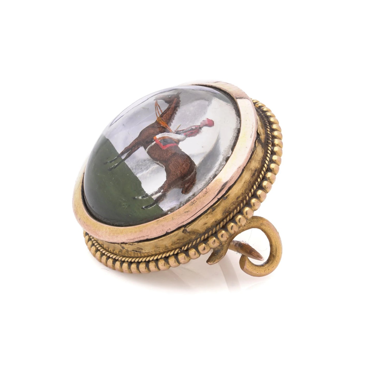 A round crystal brooch in yellow gold featuring a jockey sitting on a horse's back, on a white background