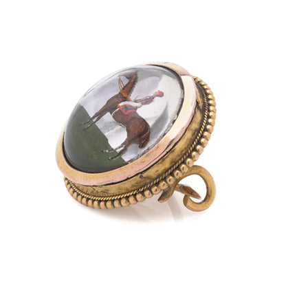 A round crystal brooch in yellow gold featuring a jockey sitting on a horse's back, on a white background