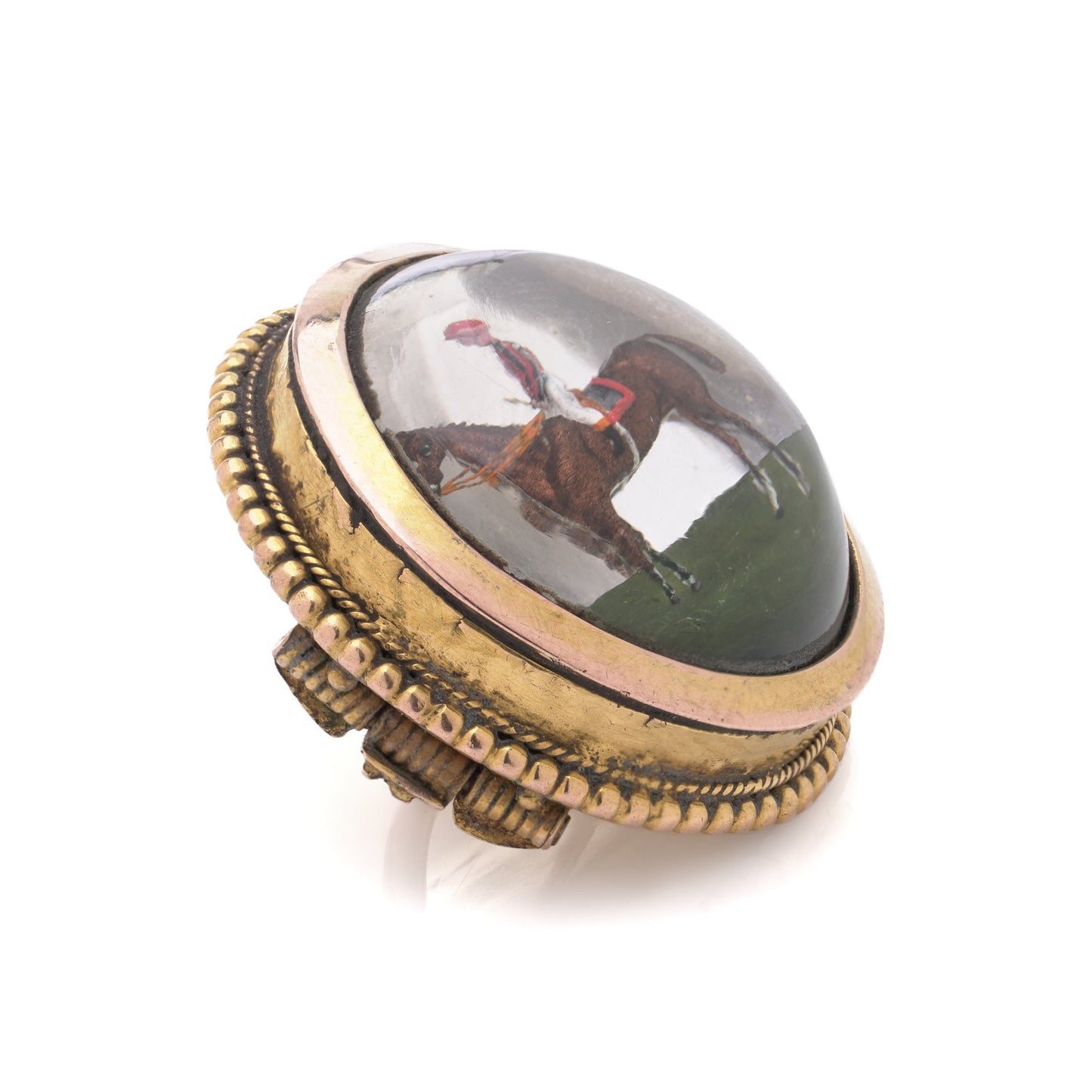 A round crystal brooch in yellow gold featuring a jockey sitting on a horse's back, on a white background