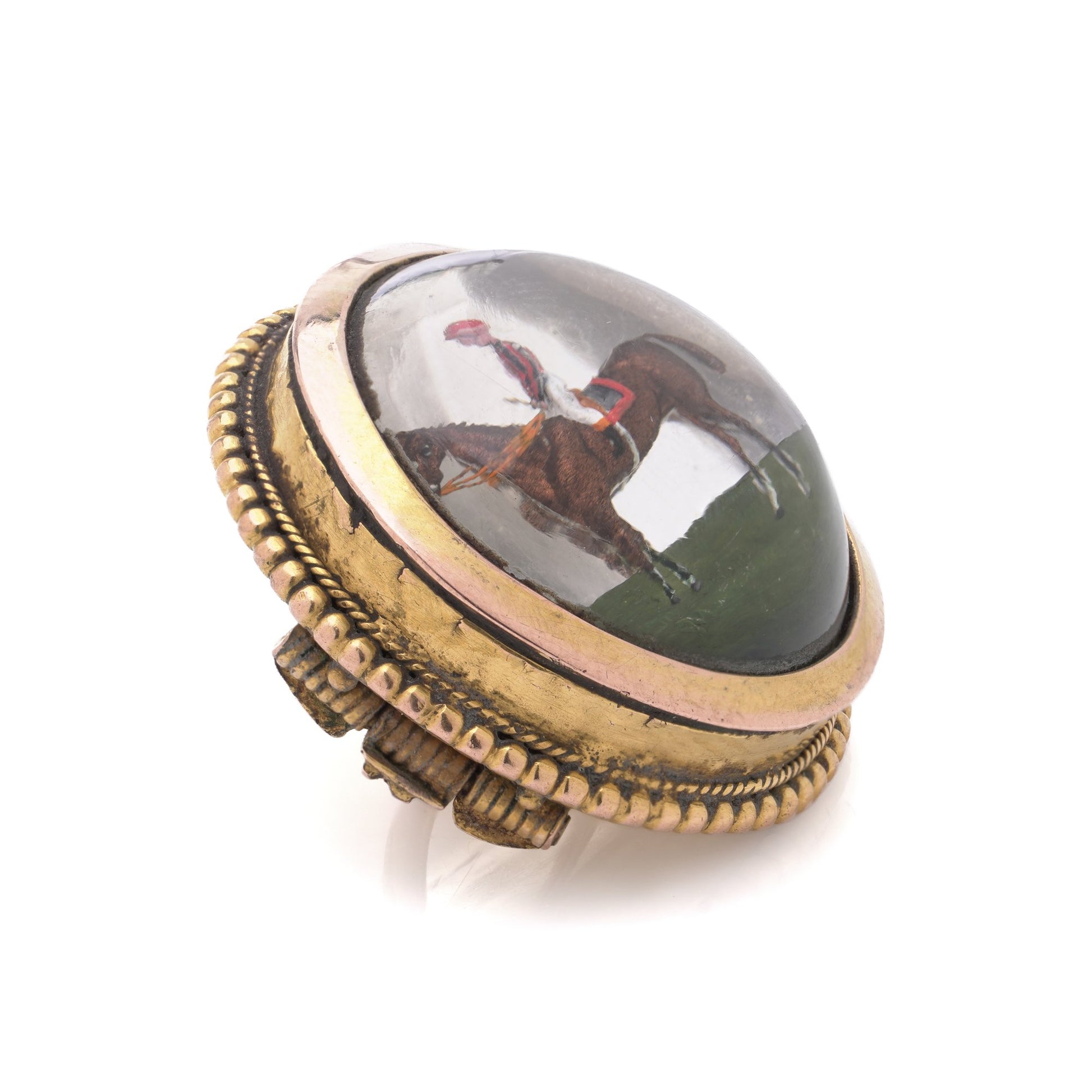 A round crystal brooch in yellow gold featuring a jockey sitting on a horse's back, on a white background
