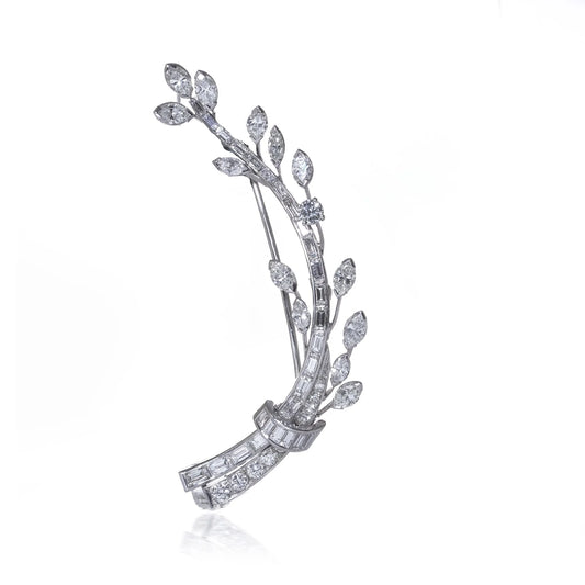 A leaf design brooch set with baguette, marquise and brilliant cut diamonds in white metal, on a white background