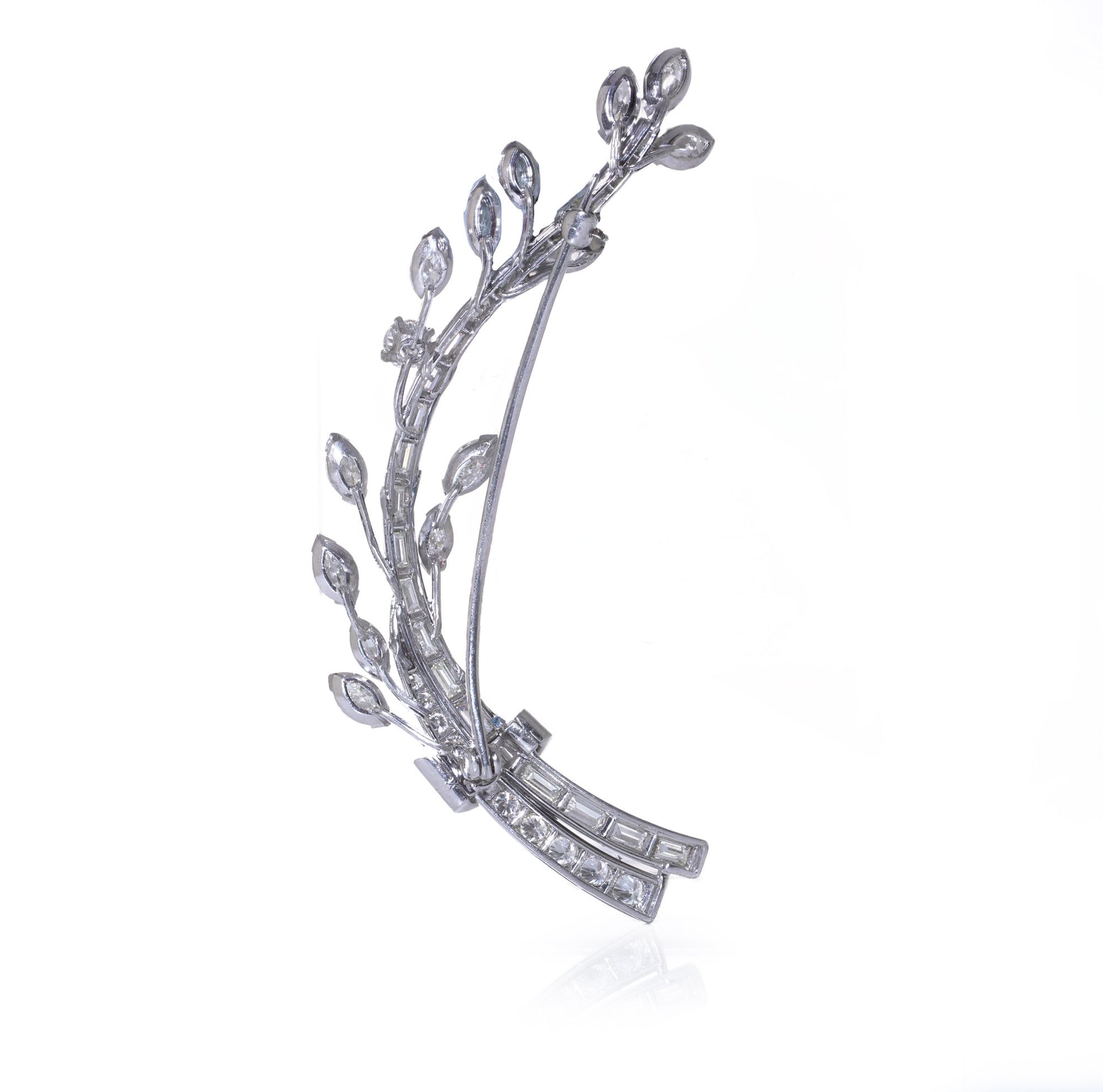 A leaf design brooch set with baguette, marquise and brilliant cut diamonds in white metal, on a white background