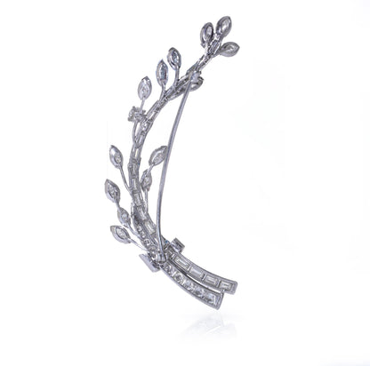A leaf design brooch set with baguette, marquise and brilliant cut diamonds in white metal, on a white background
