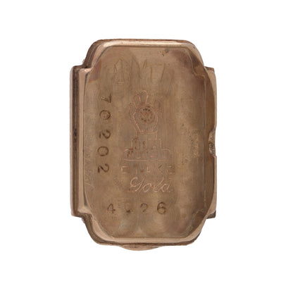 A yellow gold watch case back stamped with serial numbers, on a white background