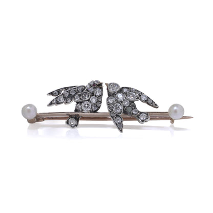 An antique bar brooch with two diamond set swallow birds, in gold and silver with pearls, on a white background