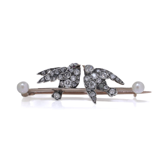 An antique bar brooch with two diamond set swallow birds, in gold and silver with pearls, on a white background