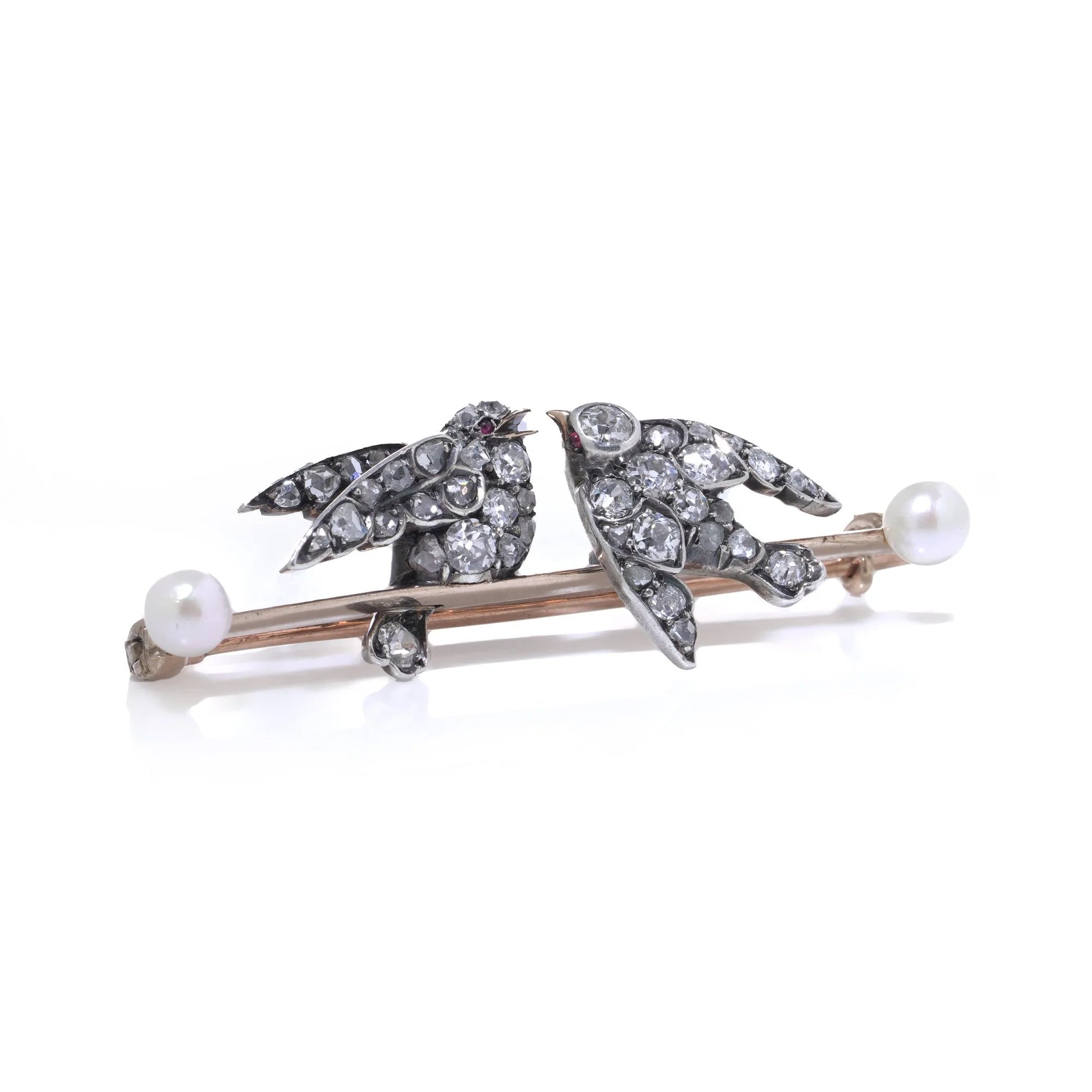An antique bar brooch with two diamond set swallow birds, in gold and silver with pearls, on a white background