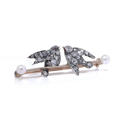 An antique bar brooch with two diamond set swallow birds, in gold and silver with pearls, on a white background