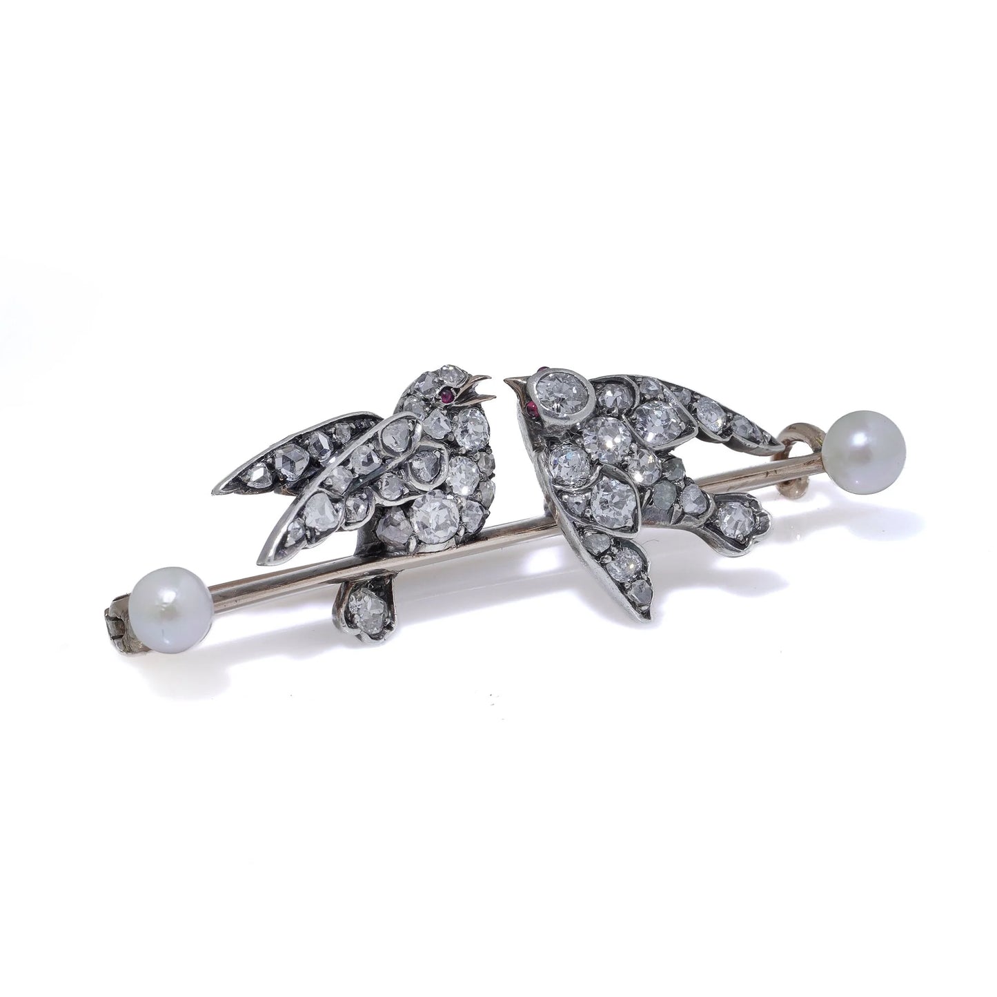 An antique bar brooch with two diamond set swallow birds, in gold and silver with pearls, on a white background