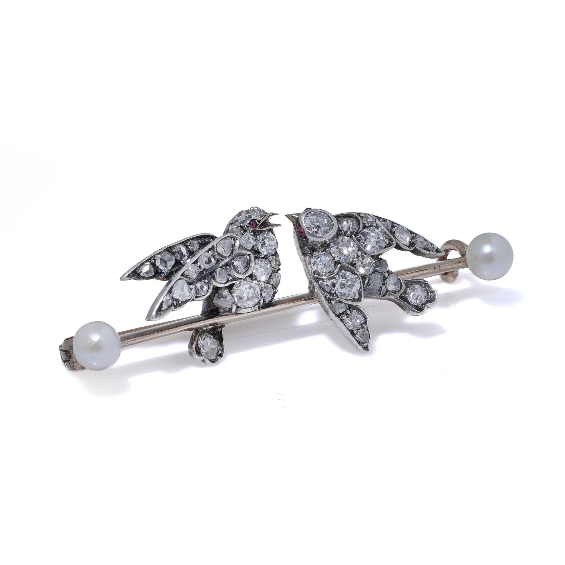 An antique bar brooch with two diamond set swallow birds, in gold and silver with pearls, on a white background
