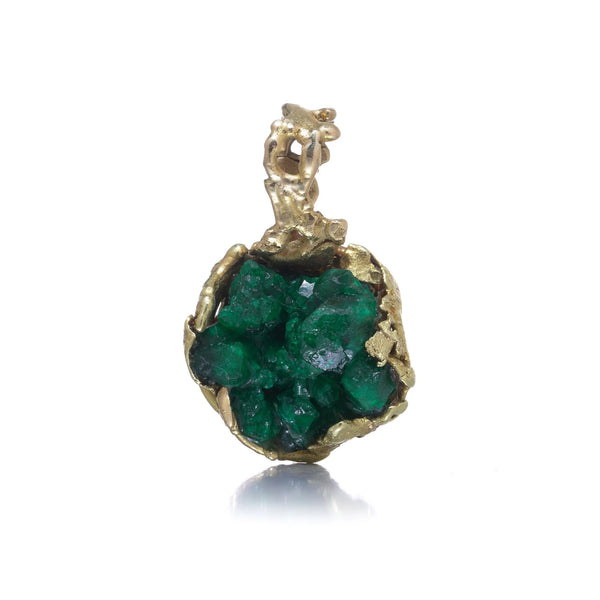 A yellow gold free-form pendant with a rough cut emerald, on a white background