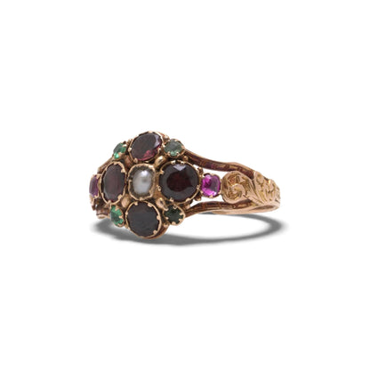 An antique gold ring with garnets, amethysts, green stones and a pearl, with decorative shoudlers, on a white background