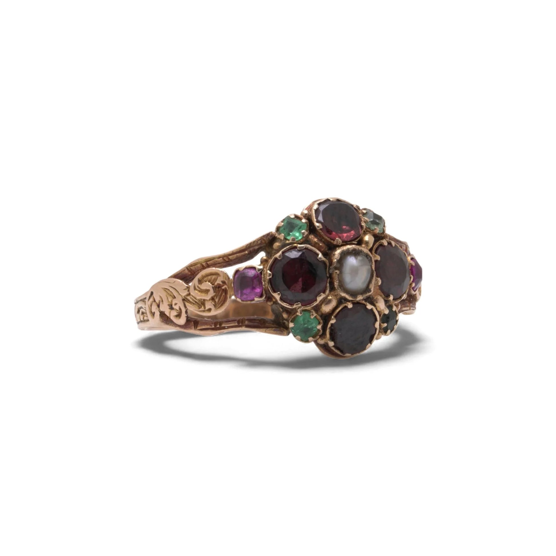 An antique gold ring with garnets, amethysts, green stones and a pearl, with decorative shoudlers, on a white background