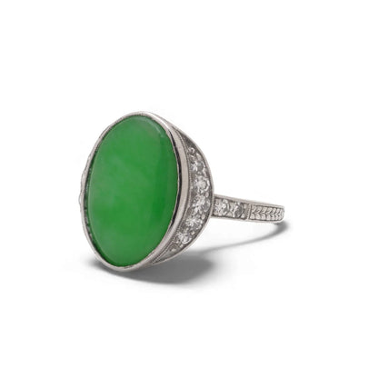 An Art Nouveau oval jade and diamond ring in platinum, against a white background