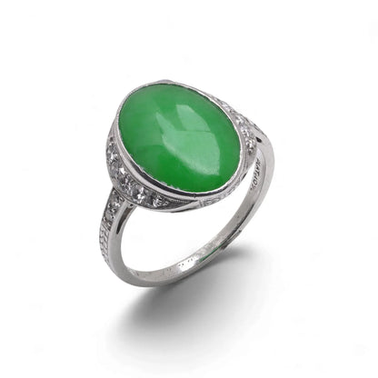 An Art Nouveau oval jade and diamond ring in platinum, against a white background