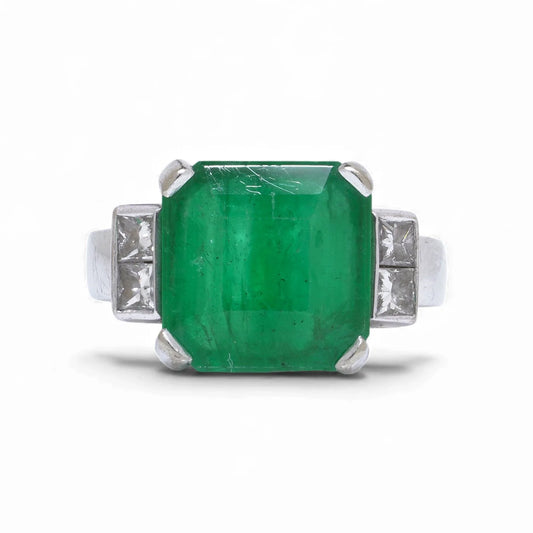 An emerald and square diamond five stone ring in white gold, on a white background
