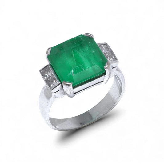 An emerald and square diamond five stone ring in white gold, on a white background