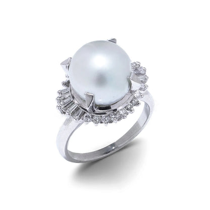 A platinum ring featuring a large white pearl surrounded by baguette and brilliant cut diamonds, on a white background