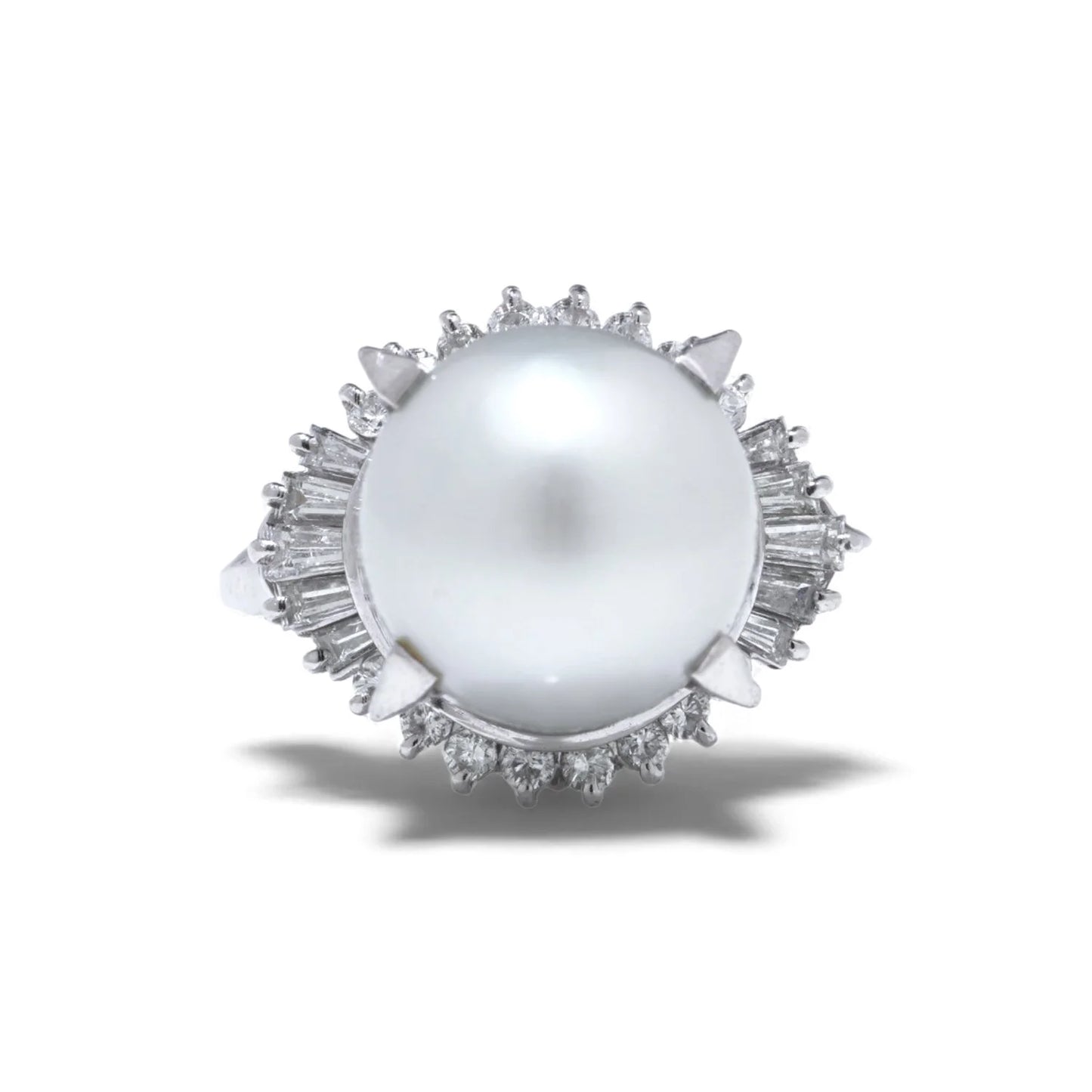 A platinum ring featuring a large white pearl surrounded by baguette and brilliant cut diamonds, on a white background