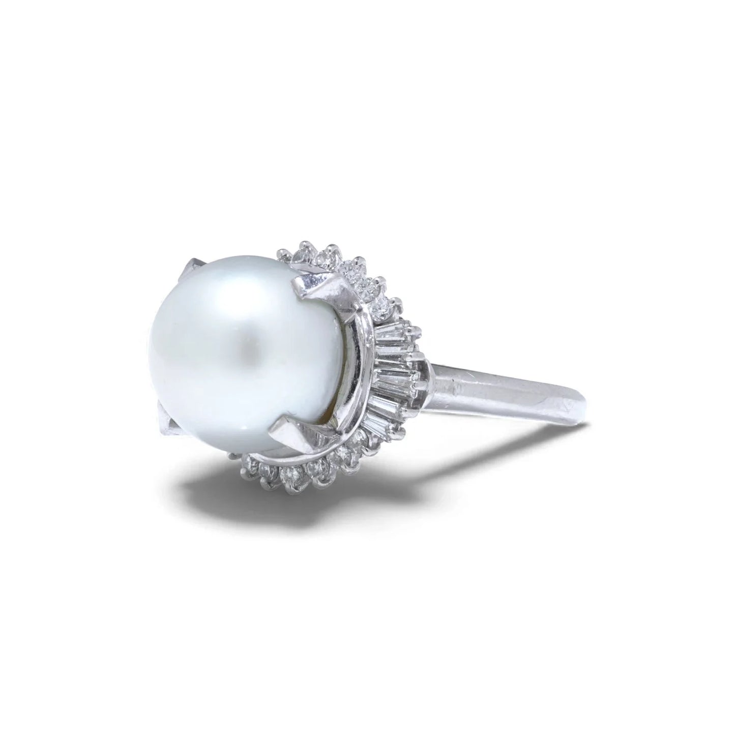 A platinum ring featuring a large white pearl surrounded by baguette and brilliant cut diamonds, on a white background