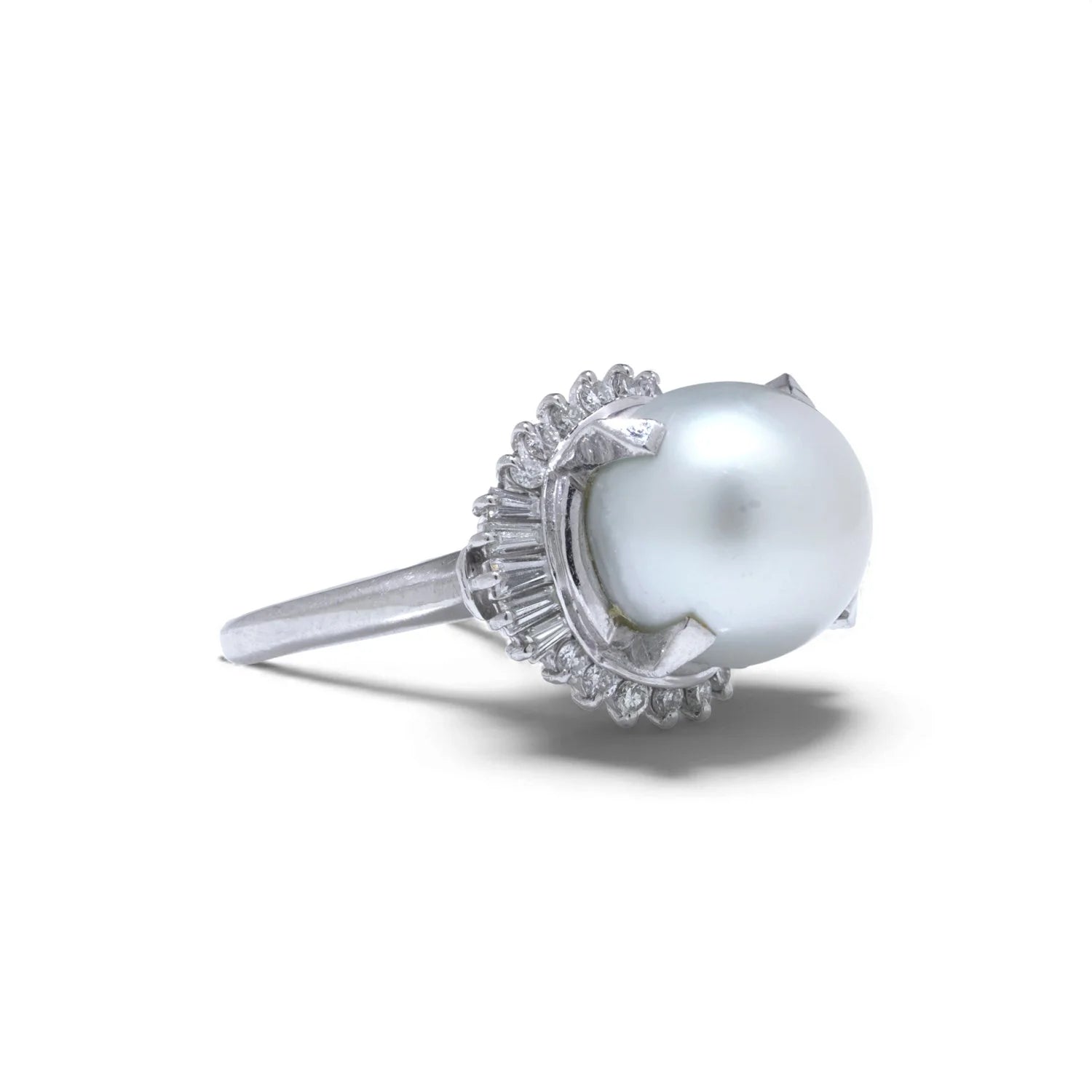 A platinum ring featuring a large white pearl surrounded by baguette and brilliant cut diamonds, on a white background