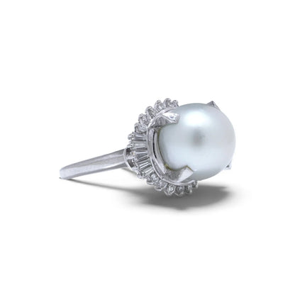 A platinum ring featuring a large white pearl surrounded by baguette and brilliant cut diamonds, on a white background