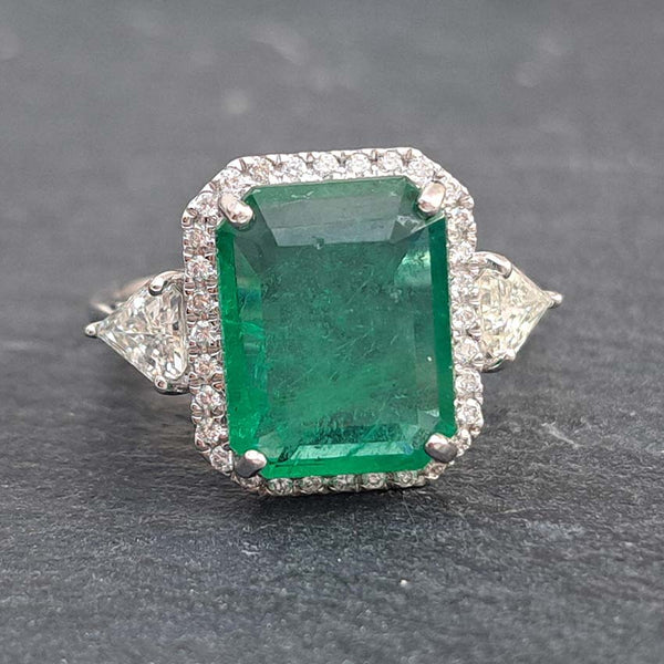 An emerald and diamond octagonal shaped cluster ring with trilliant cut diamond shoulders in white metal, on a grey slate background
