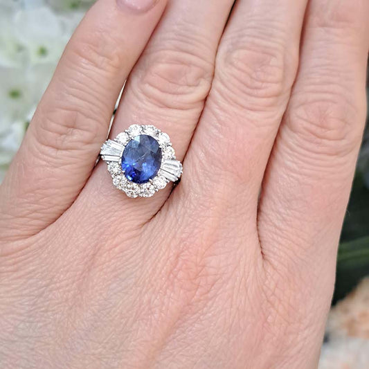 An oval sapphire, brilliant cut and baguette cut diamond cluster ring in white gold, modelled on a hand