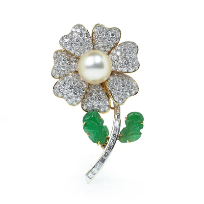 A flower brooch set with diamonds, a pearl centre and emerald leaves, in yellow and white gold