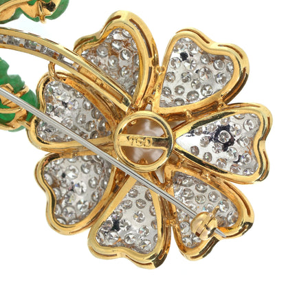 A flower brooch set with diamonds, a pearl centre and emerald leaves, in yellow and white gold
