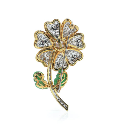 A flower brooch set with diamonds, a pearl centre and emerald leaves, in yellow and white gold