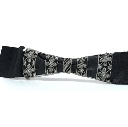 A floral design diamond and platinum bow brooch with a black ribbon