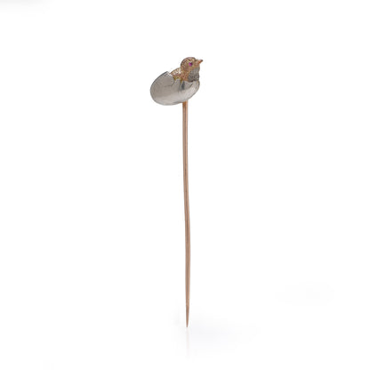 A stick pin depicting a chick hatching from an egg, in gold and silver