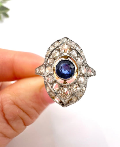 A sapphire and diamond openwork ring in platinum with a yellow gold ring shank, held in a hand