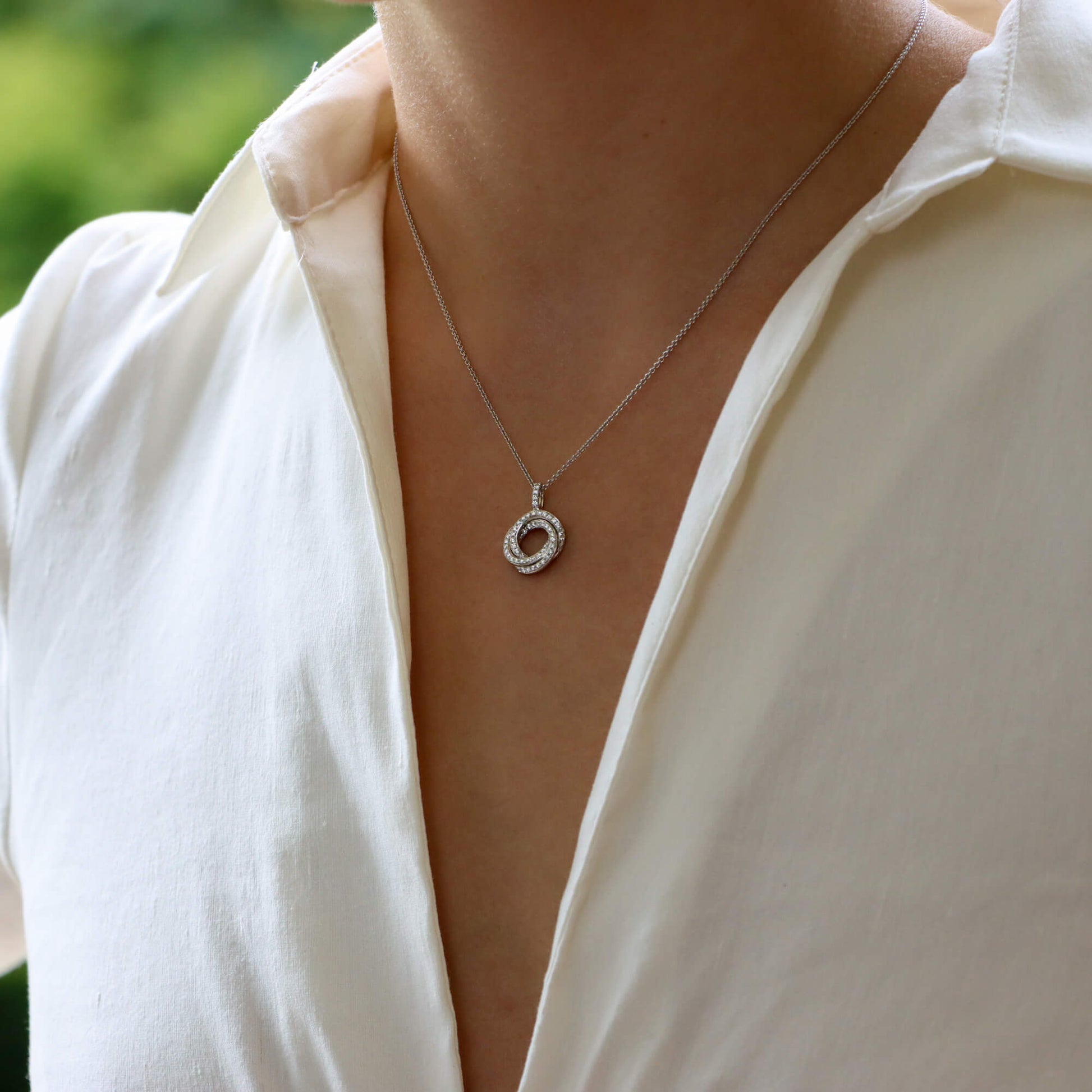 A white gold diamond set open circle pendant on a white gold chain, modelled by a woman wearing a white shirt