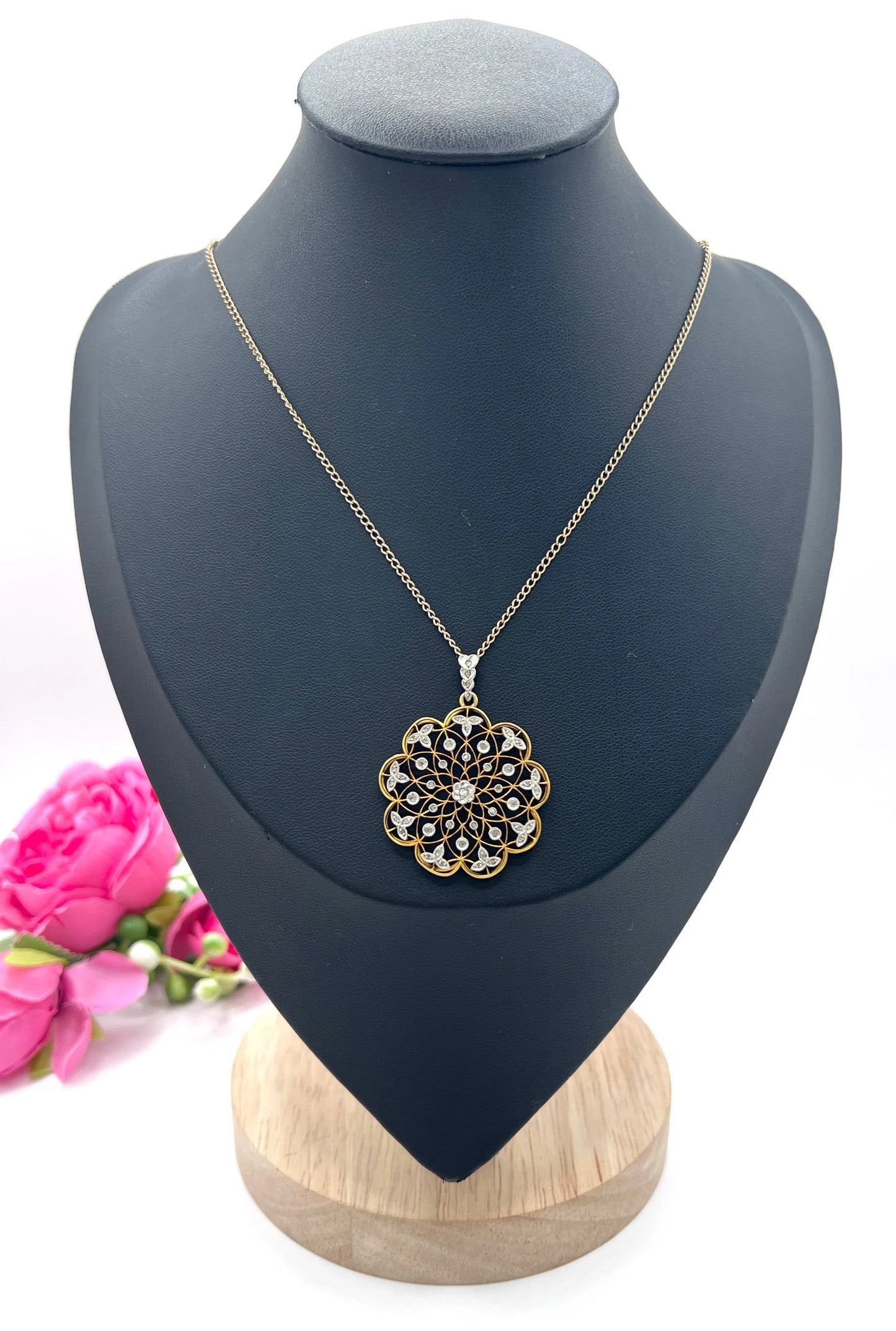 A floral openwork diamond pendant in gold and platinum, with a chain, on a black jewellery bust
