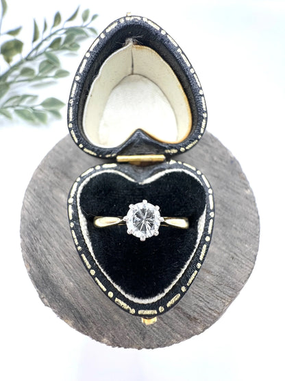A single stone brilliant cut diamond ring claw set in platinum and yellow gold, in a heart-shaped ring box