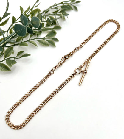 A gold curb link Albert chain, laid on a white background