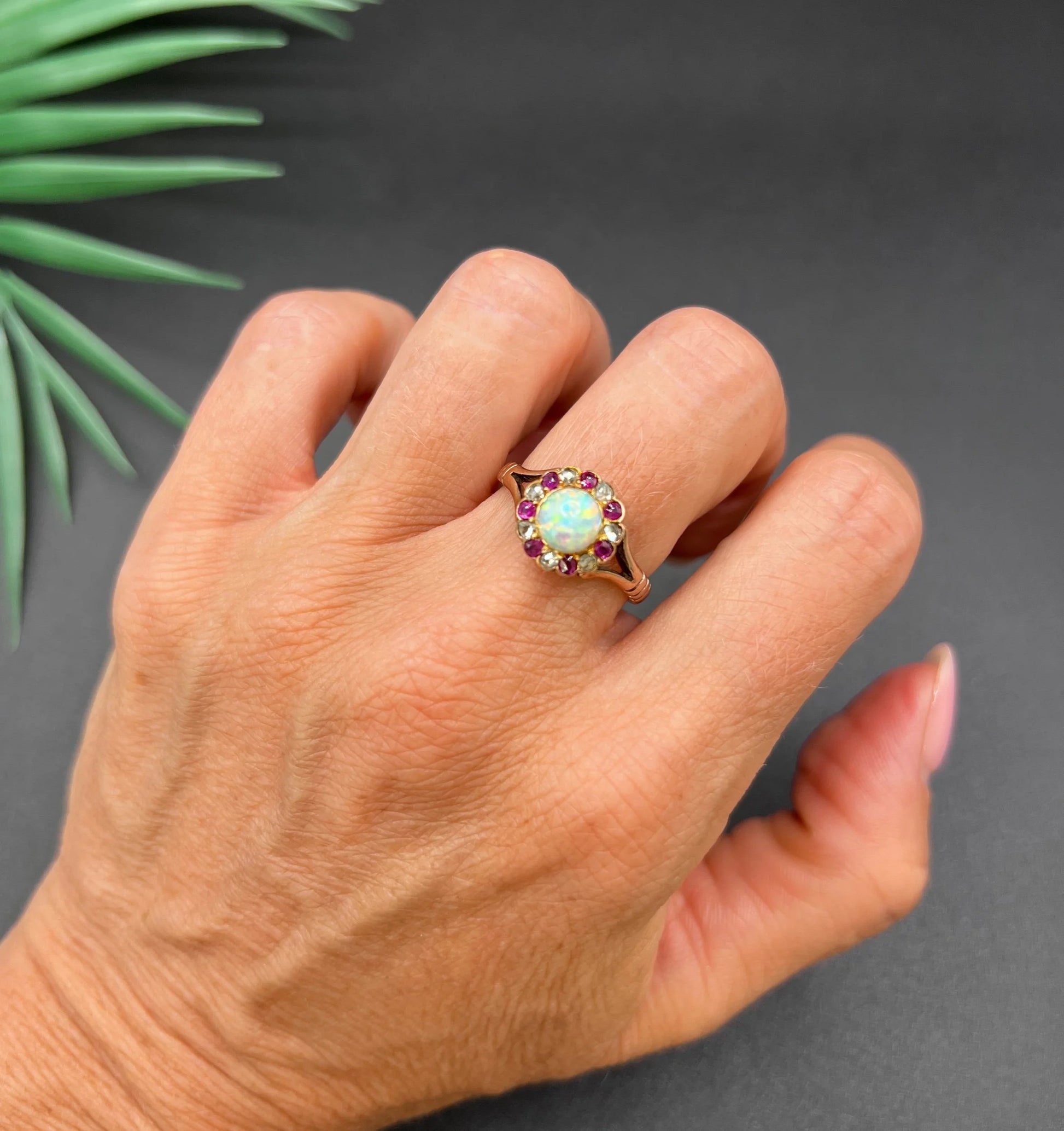 A daisy style cluster ring in rose gold with opal, ruby and diamond, modelled on a hand