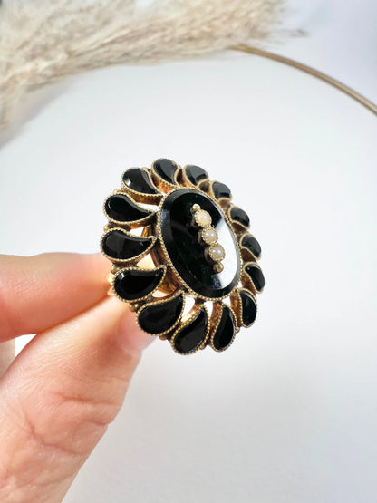 A black onyx and seed pearl fancy halo cluster ring in yellow gold, held in a hand