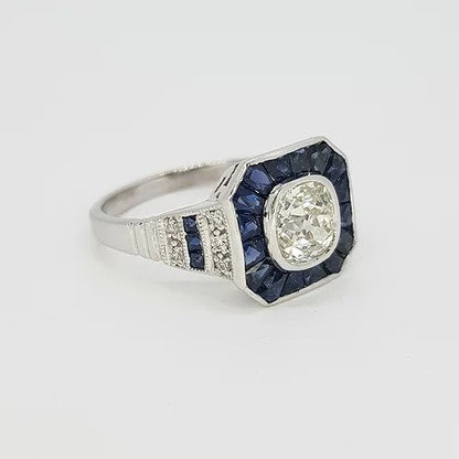 Sapphire and Diamond Calibre Cluster Target Ring; central 1.20 carat brilliant cut diamond surrounded by calibre cut sapphires, diamonds and sapphires set to the shoulders, in 18ct white gold. Reminiscent of the Art Deco style
